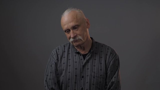 embarrassed elderly man with long grey mustache expresses shy emotions looks down and at camera close view. Concept man emotion