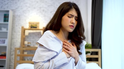 Portrait of 20s young Asian woman having difficulty breathing in bedroom at night. Shortness of breath, asthma, difficult to breathe problems. Corona Virus symptoms.