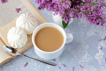 Coffee or tea with milk and marshmallows. Reading a book in the garden with a cup of coffee. Romantic still life with lilac flowers.