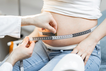 Doctor measuring pregnant woman's belly with a tape during a medical examination, cropped view without face focused on the abdomen