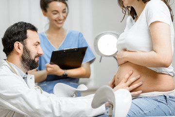 Obraz premium Male doctor with a nurse during a medical examination of a pregnant woman in the office. Concept of medical care and health during a pregnancy