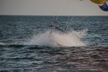A young man and a girl are flying on a double parachute behind a boat over the sea.