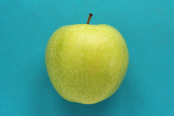 Green yellow apple on a blue background. Juicy ripe beautiful fruit.