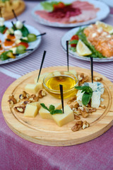 Wood board with assortment of cheese, nuts and honey on dinner table. Cheese plate