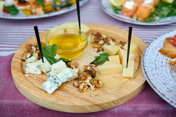 Wood board with assortment of cheese, nuts and honey on dinner table. Cheese plate