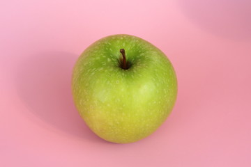 Green yellow apple on a pink background. Juicy ripe beautiful fruit.