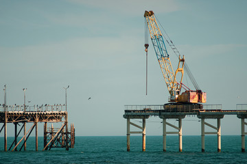 Crane building a fishing pier in turqoise water and demolishing the old one