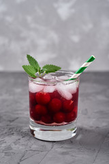 Fresh cherry lemonade with ice, mint and paper straw in sparkling glass on gray table background, copy space. Cold summer drink. Berry cocktail