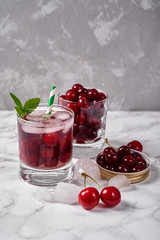 Fresh cherry lemonade with ice, mint and paper straw in sparkling glasses on table, copy space. Cold summer drink. Berry cocktail