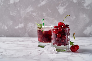 Fresh cherry lemonade with ice, mint and paper straw in sparkling glasses on table, copy space. Cold summer drink. Berry cocktail