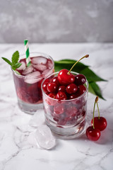 Fresh cherry lemonade with ice, mint and paper straw in sparkling glasses on table, copy space. Cold summer drink. Berry cocktail