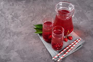 Fresh cherry lemonade in glasses with paper straws and jug on gray table background, copy space. Cold summer drink. Berry cocktail