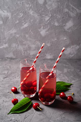 Fresh cherry lemonade with paper straw in glass on table, copy space. Cold summer drink. Sparkling glasses with berry cocktail