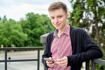 Portrait of happy young student walking in park, listening to music with earphones and using mobile smartphone outdoors, copy space