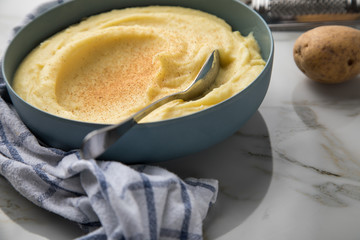 Schale Schüssel mit Kartoffelpüree mit Zutaten aus Kartoffeln, Muskatnuss dazu Küchentuch und Muskatreibe auf hell Marmor Hintergrund