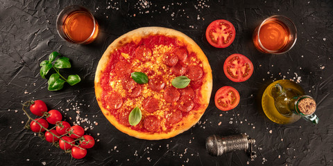 Pepperoni pizza panorama on a dark background, with wine and ingredients, tomatoes, basil, and olive oil, overhead shot