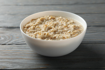 Bowl with oatmeal porridge on wooden background