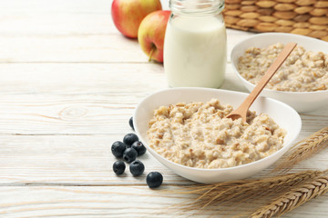 Composition with oatmeal porridge on white wooden background. Cooking breakfast