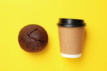 Paper cup and chocolate muffin on yellow background, space for text