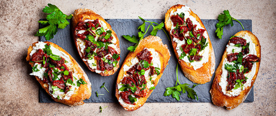 Toasts with sun-dried tomatoes and cream cheese on black board, dark background, top view.