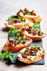 Toasts with sun-dried tomatoes and cream cheese on black board, dark background.