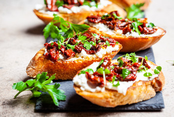 Toasts with sun-dried tomatoes and cream cheese on black board, dark background.