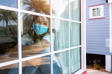 Coronavirus. Sick woman of corona virus looking through the window and wearing mask protection and recovery from the illness in home. Quarantine. Patient isolated to prevent infection. new normal..
