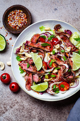 Thai beef salad with vegetables and nuts in a white bowl on dark background, top view. Asian food concept.