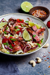 Thai beef salad with vegetables and nuts in a white bowl on dark background. Asian food concept.