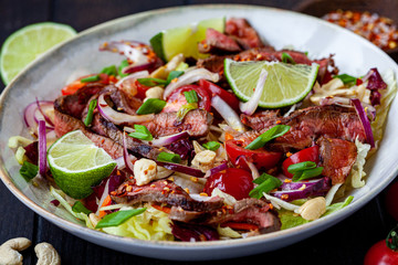 Thai beef salad with vegetables and nuts in a white bowl on dark background. Asian food concept.