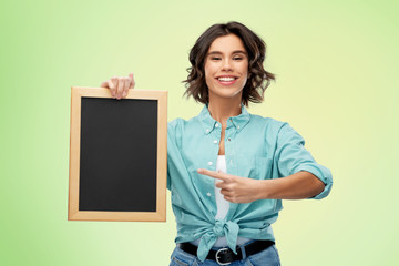 people concept - portrait of happy smiling young woman in turquoise shirt showing black chalkboard...