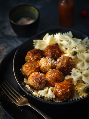 Farfalle pasta with chicken meatballs in tomato sauce, on a dark background