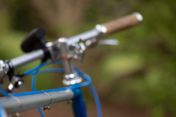 Fototapeta na wymiar Detail of a beautiful customized retro bicycle focusing on the handlebar with a blurry park and trees in the background