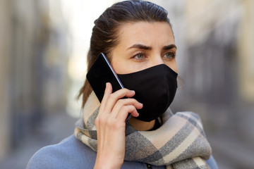 health, safety and pandemic concept - young woman wearing black face protective reusable barrier mask outdoors calling on smartphone