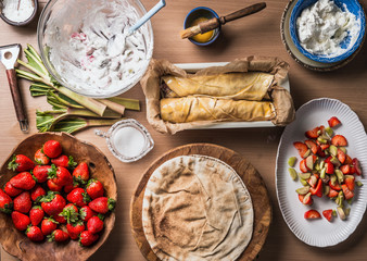 Strawberry rhubarb wrap cake  preparation made without dough , but with flatbread on wooden kitchen table background with bowls with ingredients. Top view. Flat lay food