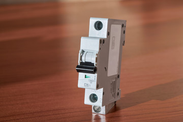 Electric single-pole modular circuit breaker on the table surface in red color. The switch has a green pin status indicator. The switch lever is black. Protection of electrical wiring in the building.