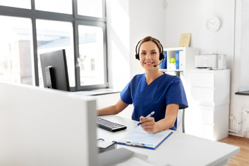 Obraz na płótnie Canvas medicine, technology and healthcare concept - happy smiling female doctor or nurse with headset and computer working at hospital