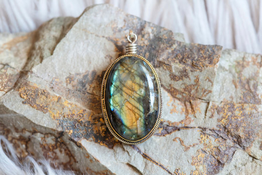 Brass pendant with natural labradorite gemstone on rocky background