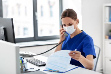 medicine, people and healthcare concept - female doctor or nurse wearing face protective medical mask for protection from virus disease with computer and clipboard calling on phone at hospital - obrazy, fototapety, plakaty