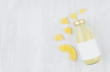Bright pinapple yellow juice in glass bottle with blank label, sliced fruit on white wooden board, top view, copy space, template for design, advertising, portfolio.