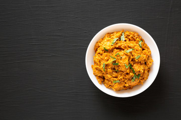 Homemade Chicken Tikka Masala in a white bowl on a black background, top view. Flat lay, overhead, from above. Copy space.