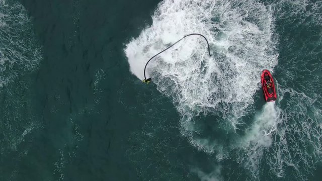 A man demonstrating a flyboard and a red motorboat.