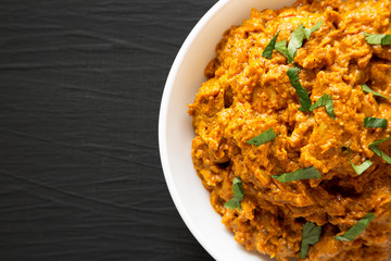 Homemade Chicken Tikka Masala in a white bowl on a black background, top view. Flat lay, overhead, from above. Copy space.