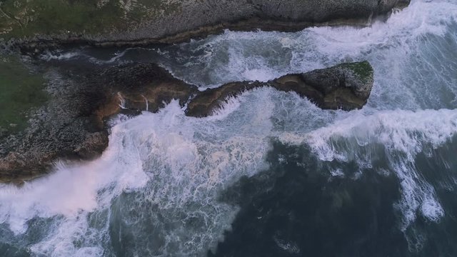 AERIAL DRONE TOP DOWN OD ROCKY CLIFFS WITH BIG WAVES IN NORTHERN SEA COAST
