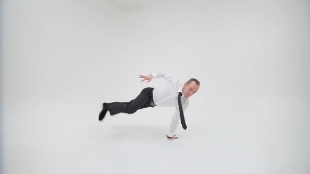 Office clerk dancing bottom break on a white background. A happy businessman is dancing a break dance and spinning on his hands. A guy in office clothes is spinning on his hands swinging his legs