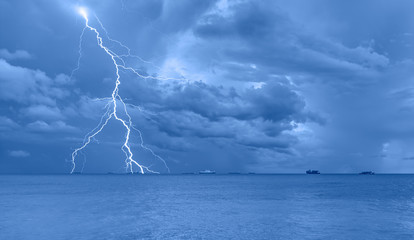 Many cargo ships waiting in the middle of the sea to unload cargo with lightning in dark sky and...