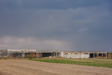 Ruins of an industrial building on a background of stormy sky. Sown fields in the foreground