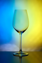 The crystal glass stands on the reflecting surface on a yellow blue background. studio photo. product. Beautiful shadow from wine glass. macro photo