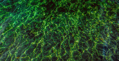 Water background. Ripples on green transparent water in sea with sun reflection. Top view. Abstract texture and structure.
