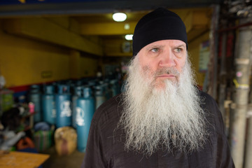 Stressed mature bearded hipster man in front of gas tanks outdoors